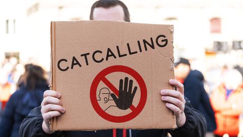 Ein Demonstrant hält ein Pappschild mit einem Stopp-Symbol und der Aufschrift: Catcalling