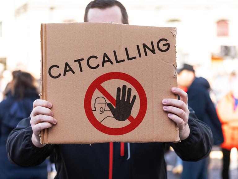 Ein Demonstrant hält ein Pappschild mit einem Stopp-Symbol und der Aufschrift: Catcalling
