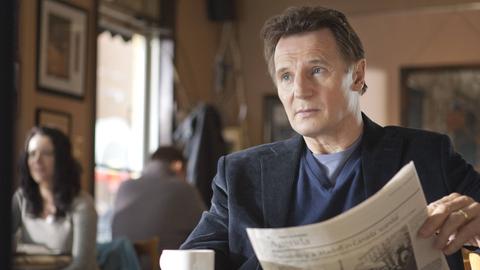 Filmausschnitt von Liam Neeson in "Chloe" wie er in einem Café sitzt und Zeitung liest.