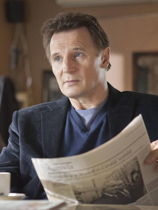 Filmausschnitt von Liam Neeson in "Chloe" wie er in einem Café sitzt und Zeitung liest.