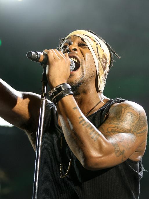 D'Angelo steht mit Mikro und ausgestrecktem Arm und Zeigefinger im Jahr 2015 in Los Angeles singend auf der Bühne.