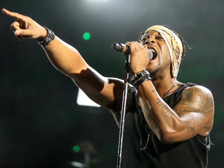 D'Angelo steht mit Mikro und ausgestrecktem Arm und Zeigefinger im Jahr 2015 in Los Angeles singend auf der Bühne.