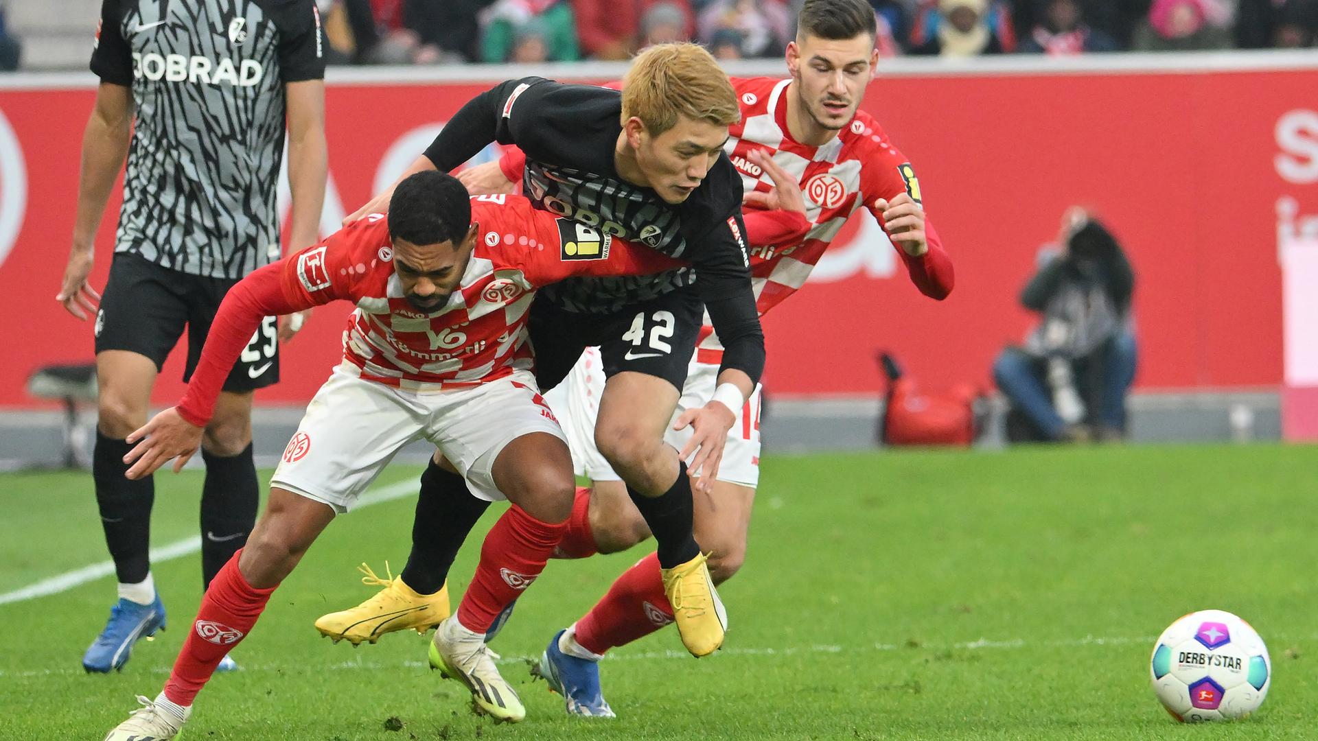 Der Freiburger Spieler Ritsu Doan versucht, an den Ball zu kommen. Er befindet sich zwei Mainzer Spielern, die das verhindern wollen.