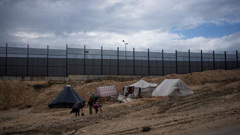 Palästinenser, die durch die israelische Luft- und Bodenoffensive auf den Gazastreifen vertrieben wurden, gehen durch ein behelfsmäßiges Zeltlager in Rafah an der Grenze zu Ägypten. Im Hintergrund ein hoher Grenzzaun.