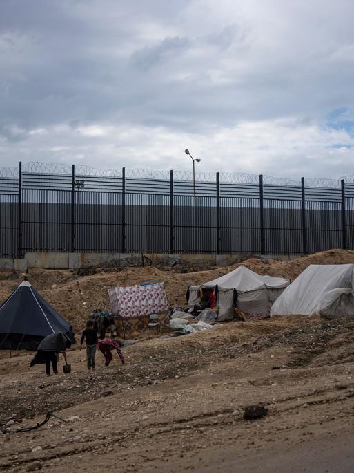 Palästinenser, die durch die israelische Luft- und Bodenoffensive auf den Gazastreifen vertrieben wurden, gehen durch ein behelfsmäßiges Zeltlager in Rafah an der Grenze zu Ägypten. Im Hintergrund ein hoher Grenzzaun.
