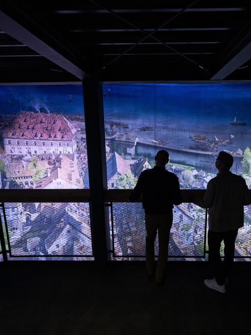 Eine Rundum-Projektion der Stadt Konstanz, wie sie im Mittelalter wohl ausgesehen haben könnte. Man sieht vor der Projekt die Silhouette von zwei Männern, die auf einer Plattform stehen und sich das Bild anschauen. Eine Rundum-Projektion der Stadt Konstanz, wie sie im Mittelalter wohl ausgesehen haben könnte. Man sieht vor der Projekt die Silhouette von zwei Männern, die auf einer Plattform stehen und sich das Bild anschauen.