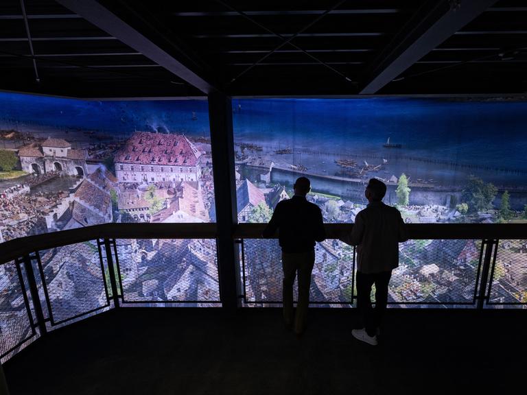 Eine Rundum-Projektion der Stadt Konstanz, wie sie im Mittelalter wohl ausgesehen haben könnte. Man sieht vor der Projekt die Silhouette von zwei Männern, die auf einer Plattform stehen und sich das Bild anschauen. Eine Rundum-Projektion der Stadt Konstanz, wie sie im Mittelalter wohl ausgesehen haben könnte. Man sieht vor der Projekt die Silhouette von zwei Männern, die auf einer Plattform stehen und sich das Bild anschauen.