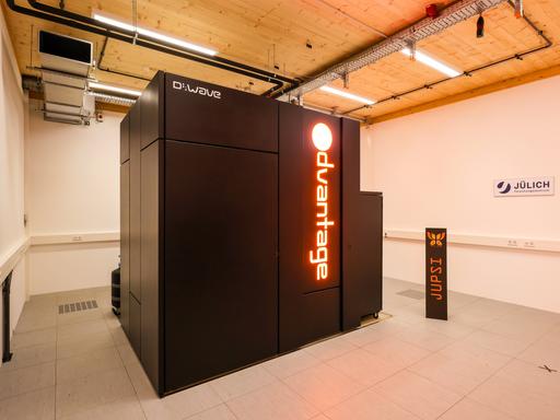 Ein schwarzer Quantencomputer steht in einem Raum mit Holzdecke im Forschungszentrum Jülich. Auf dem Computer steht in roten Leuchtbuchstaben "Advantage", der Name des Rechners.