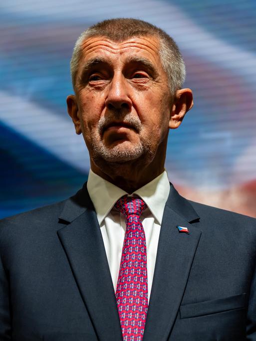 Portrait von Andrej Babiš in blauem Anzug, mit roter Krawatte vor der tschechischen Flagge