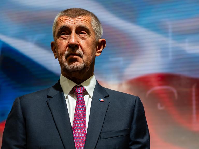 Portrait von Andrej Babiš in blauem Anzug, mit roter Krawatte vor der tschechischen Flagge