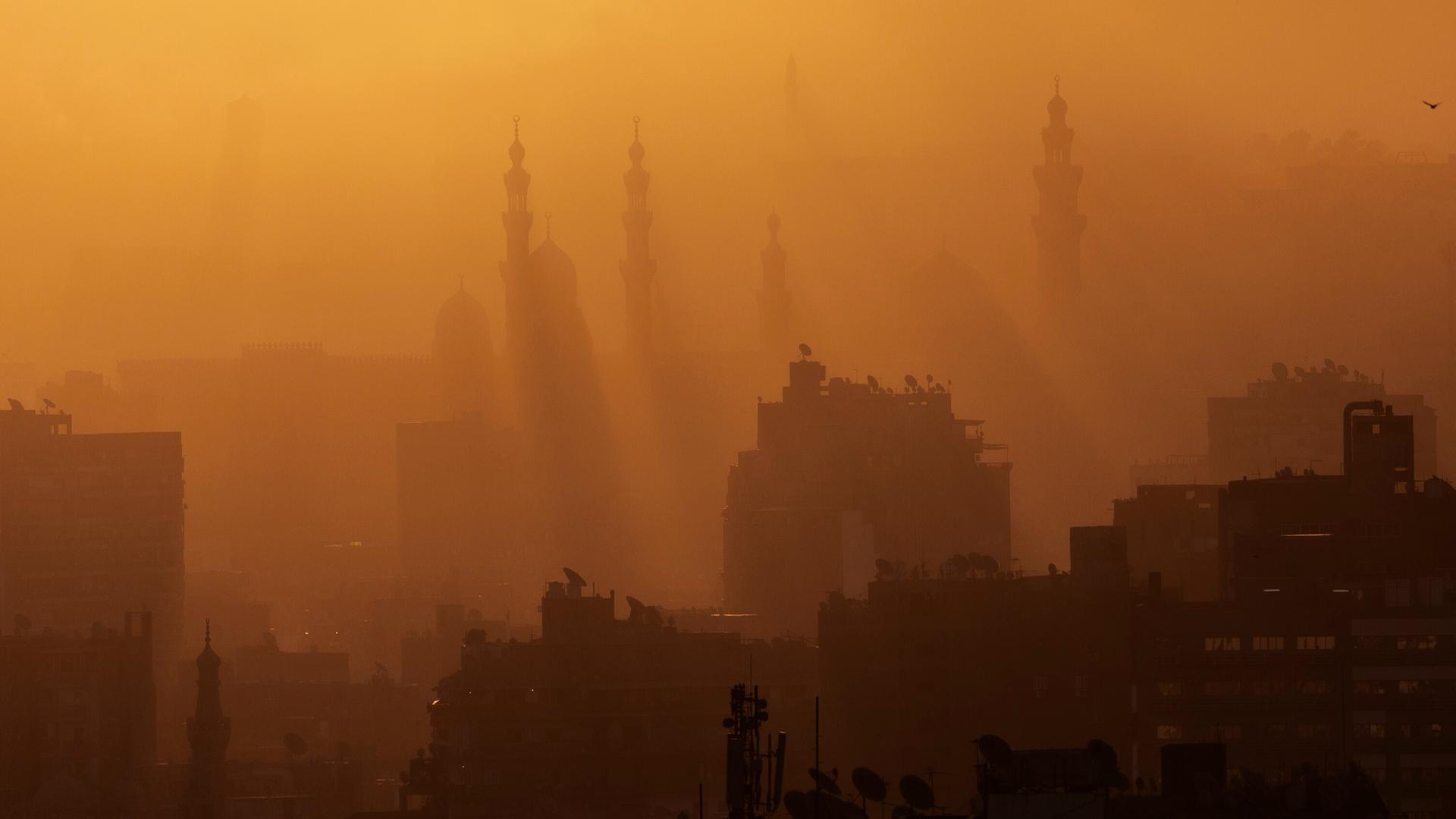 Die Sonnen scheint goldgelb durch einen diffusen Neben auf die Dächer der Stadt Kairo.