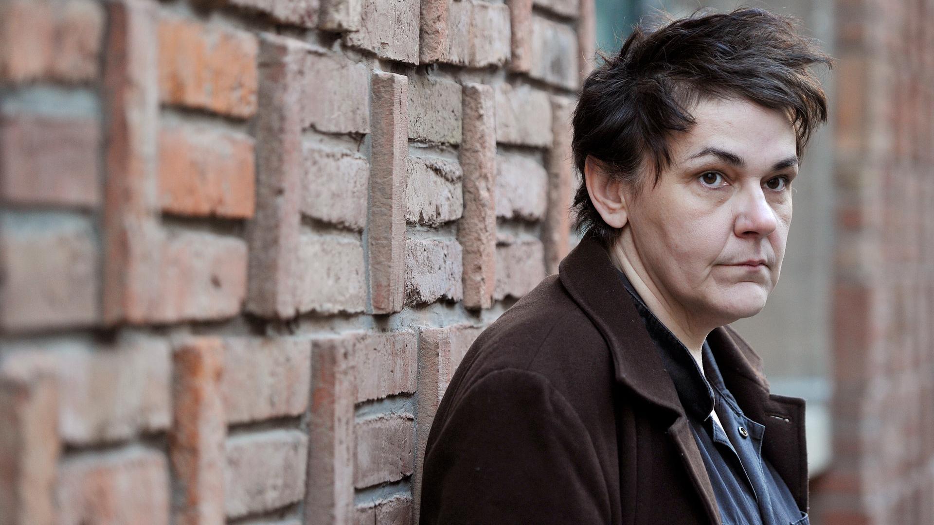 Die Sängerin Christiane Rösinge steht vor einer Wand und blickt in Richtung Kamera. Sie hat verwuscheltes Haar und trägt einen Mantel.