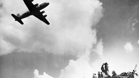 Ein Schwarzweiß-Foto zeigt Beobachter des Anflug eines Transportflugzeugs vom Typ Douglas C-54 Skymaster.