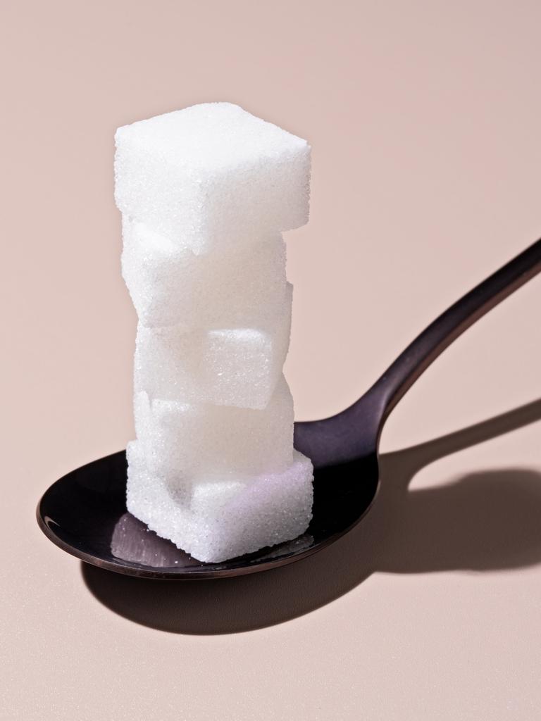 Fotografie eines schwarzen Löffel vor hellrosa Hintergrund. Auf dem Löffel stapeln sich Zuckerwürfel.