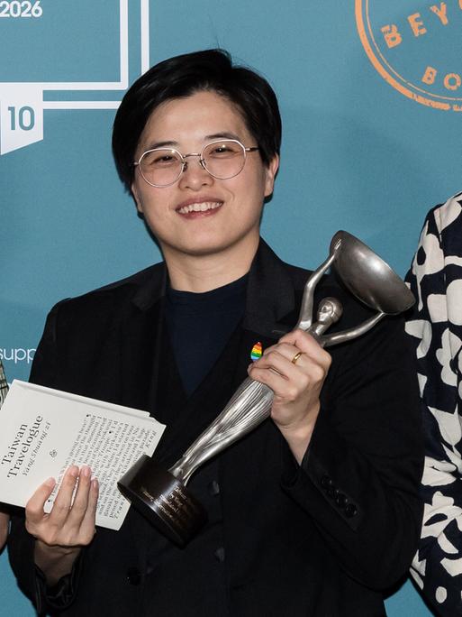 Zwei Frauen stehen nebeneinander und lächeln. Sie halten jeweils eine Statuette in silber.