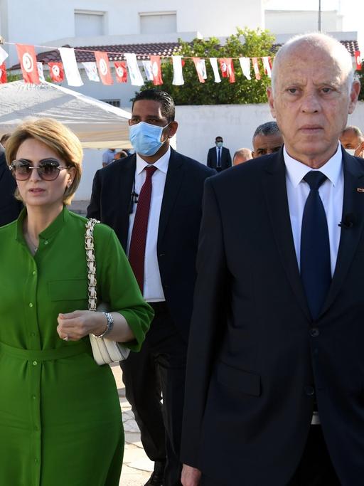 Tunesiens Präsident Kais Saied, begleitet von seiner Ehefrau und mehreren Leibwächtern, geht durch eine mit Wimpeln geschmückte Straße auf die Kamera zu.