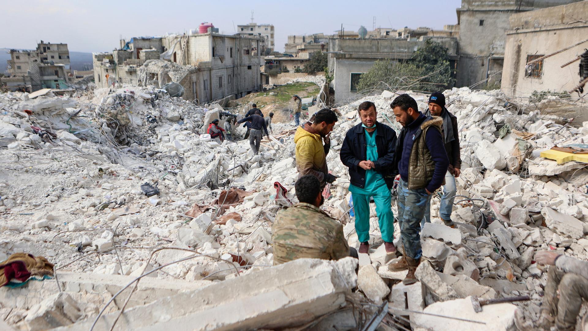 Menschen stehen auf den Trümmern von einem Haus in dem Erd-Beben-Gebiet in Syrien.
