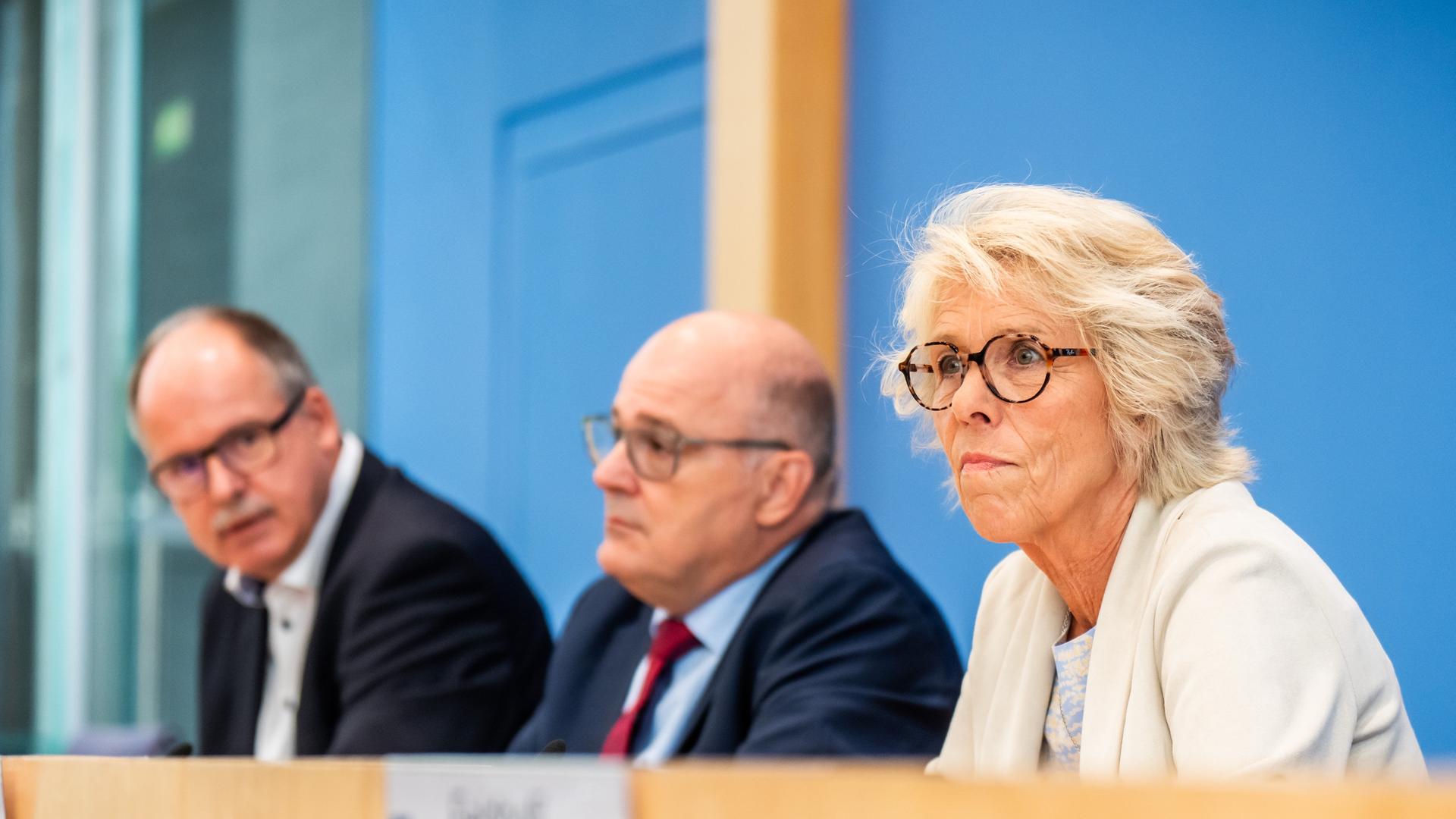 Die drei sitzen nebeneinander auf dem Podium vor der blauen Wand der Bundespressekonferenz. Sie sind schräg von der Seite fotografiert. Die drei sitzen nebeneinander auf dem Podium vor der blauen Wand der Bundespressekonferenz. Sie sind schräg von der Seite fotografiert.