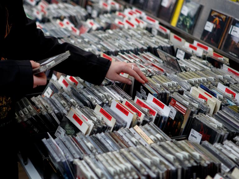 Eine Person gleitet in einem CD-Geschäft mit dem Finger durch das Angebot.