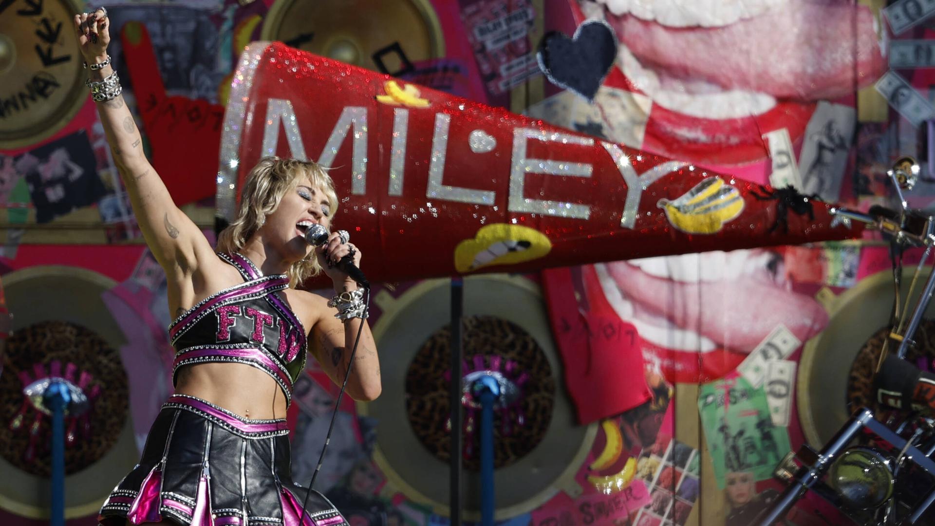 Miley Cyrus steht auf der Bühne beim TikTok-Tailgate in Tampa Bay, hinter ihr ein Schild mit der Aufschrift "Miley"