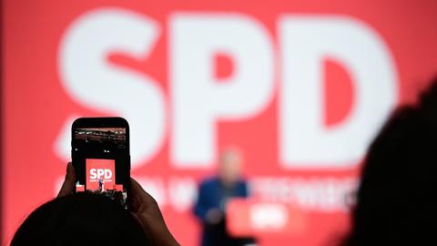 Auf einem der SPD-Parteitag filmt eine Delegierte den Redner am Rednerpult, den man im Hingtergrund unscharf unter einem großen SPD-Logo sprechen sieht. 