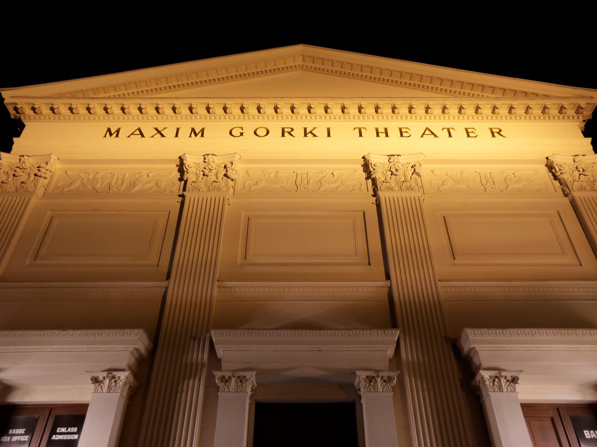 Die beleuchtete Fassade des Maxim Gorki Theaters mit klassizistischen Säulen und der Aufschrift "Maxim Gorki Theater" von unten fotografiert vor schwarzem Nachthimmel.