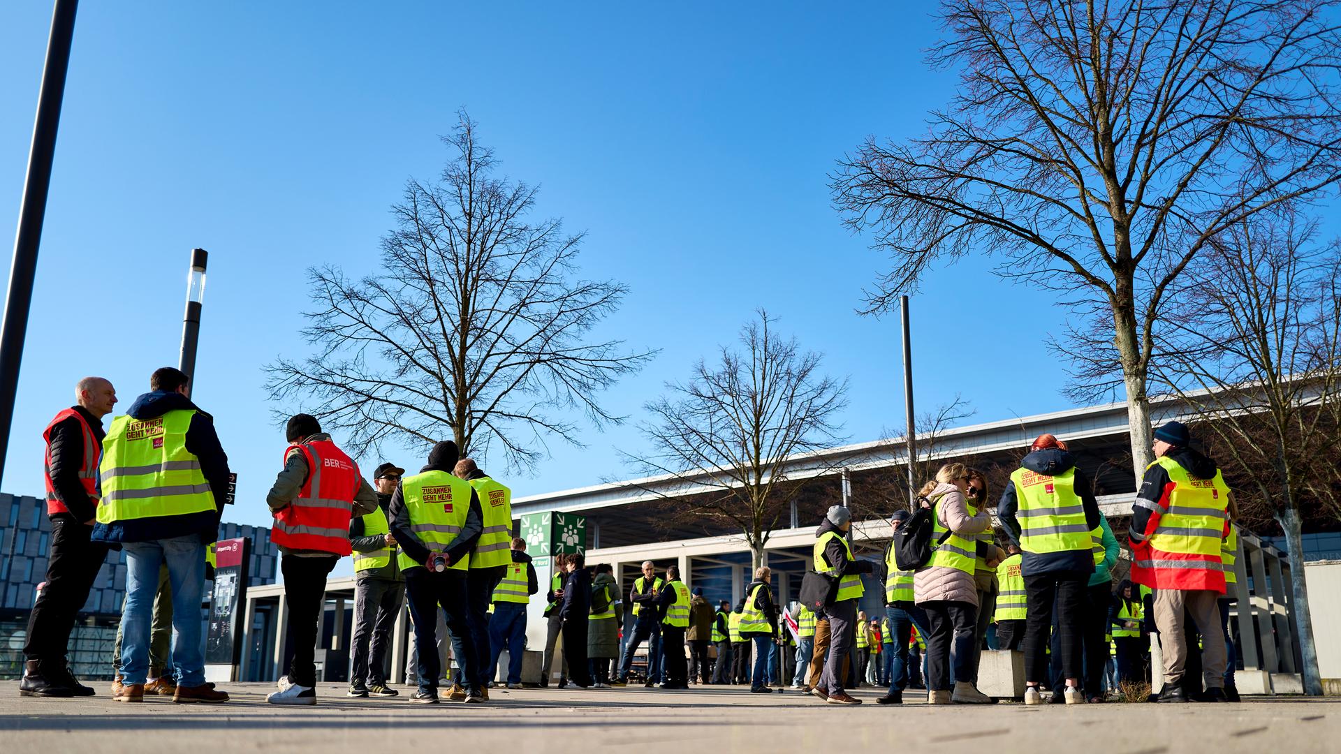 Streikende Flughafenmitarbeiter und Gewerkschaftsmitglieder stehen während eines Warnstreiks am Flughafen Berlin Brandenburg (BER) vor dem Terminal.