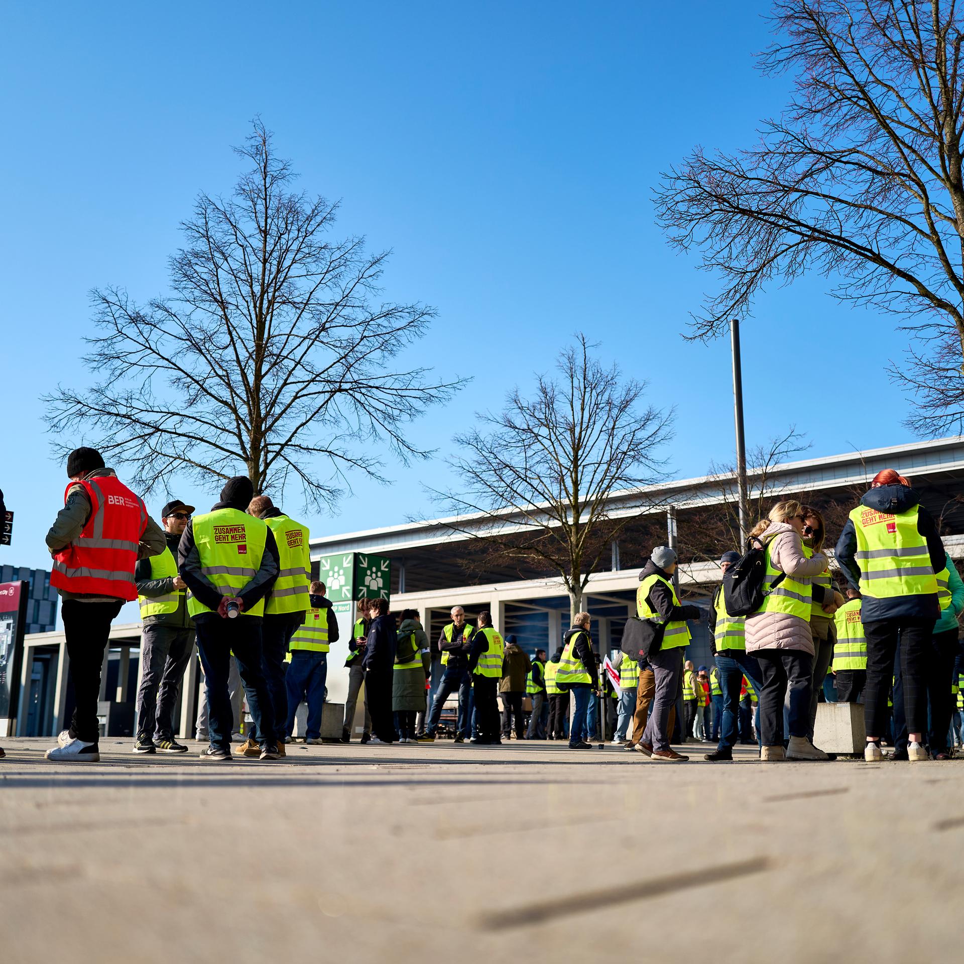 Streikende Flughafenmitarbeiter und Gewerkschaftsmitglieder stehen während eines Warnstreiks am Flughafen Berlin Brandenburg (BER) vor dem Terminal.