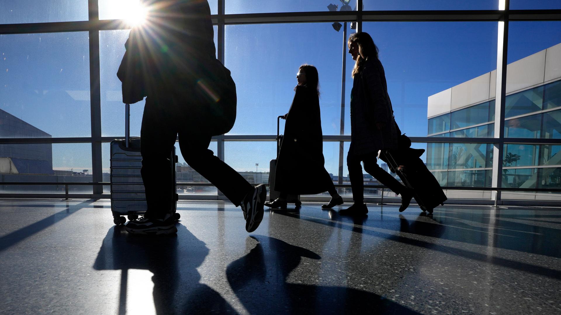 Reise schieben ihre Koffer in einem Terminal des Flughafen Boston Logan. Durch die Schreiben des Gebäudes scheint die Sonne herein. Reise schieben ihre Koffer in einem Terminal des Flughafen Boston Logan. Durch die Schreiben des Gebäudes scheint die Sonne herein.