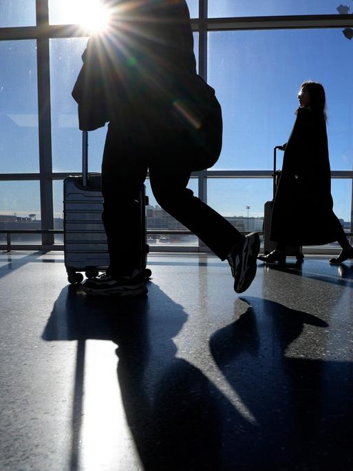 Reise schieben ihre Koffer in einem Terminal des Flughafen Boston Logan. Durch die Schreiben des Gebäudes scheint die Sonne herein.