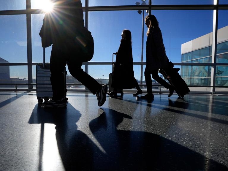Reise schieben ihre Koffer in einem Terminal des Flughafen Boston Logan. Durch die Schreiben des Gebäudes scheint die Sonne herein.