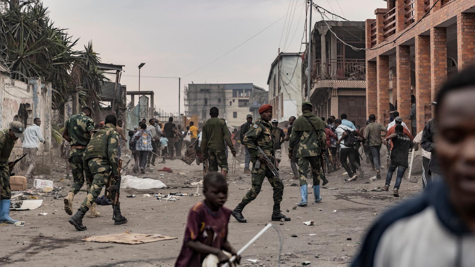 Kongolesische Soldaten gehen in der Stadt Goma gegen Demonstranten vor. Im Vordergrund läuft ein kleines Mädchen über die Straße.
