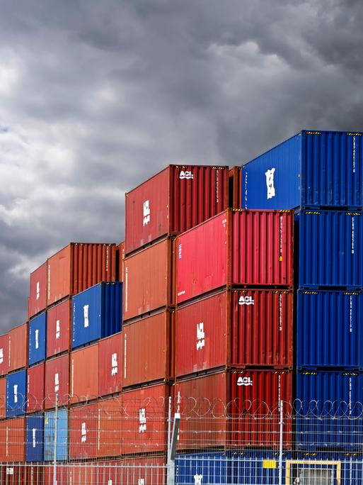 Gestapelte bunte Container im Hafengebiet von Hamburg vor dunklen Wolken