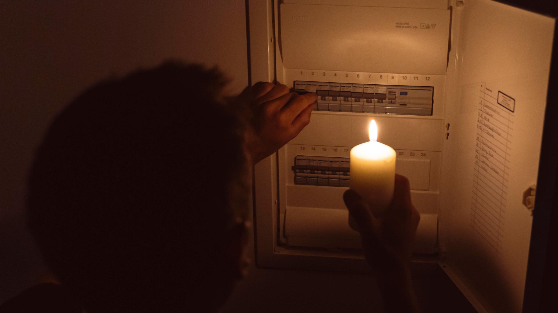Stromausfall in der Wohnung, Mann leuchtet mit Kerze und Kerzenlicht und überprüft den Sicherungskasten. Elektrizität, Strom Ausfall, Blackout Konzept