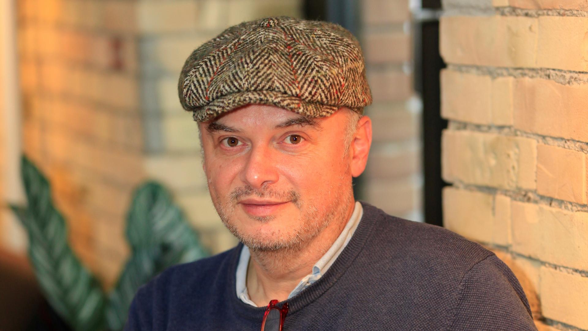 Der Schriftsteller Catalin Dorian Florescu sitzt an einem Tisch und trägt eine Schiebermütze, vor ihm mehrere Bücher. Der Schriftsteller Catalin Dorian Florescu sitzt an einem Tisch und trägt eine Schiebermütze, vor ihm mehrere Bücher.