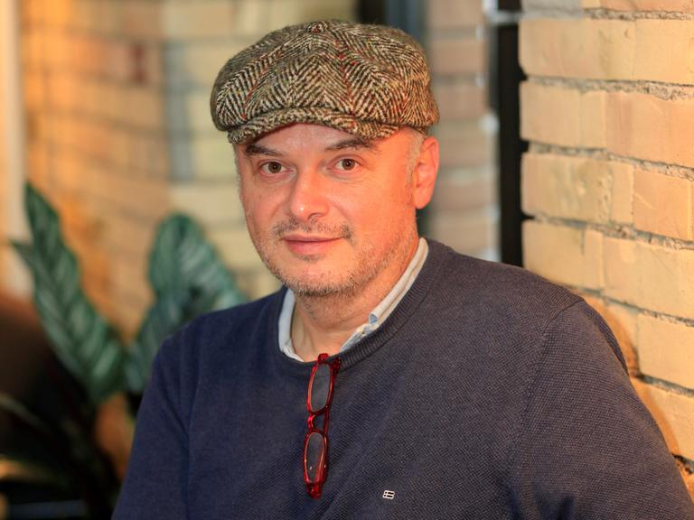 Der Schriftsteller Catalin Dorian Florescu sitzt an einem Tisch und trägt eine Schiebermütze, vor ihm mehrere Bücher.