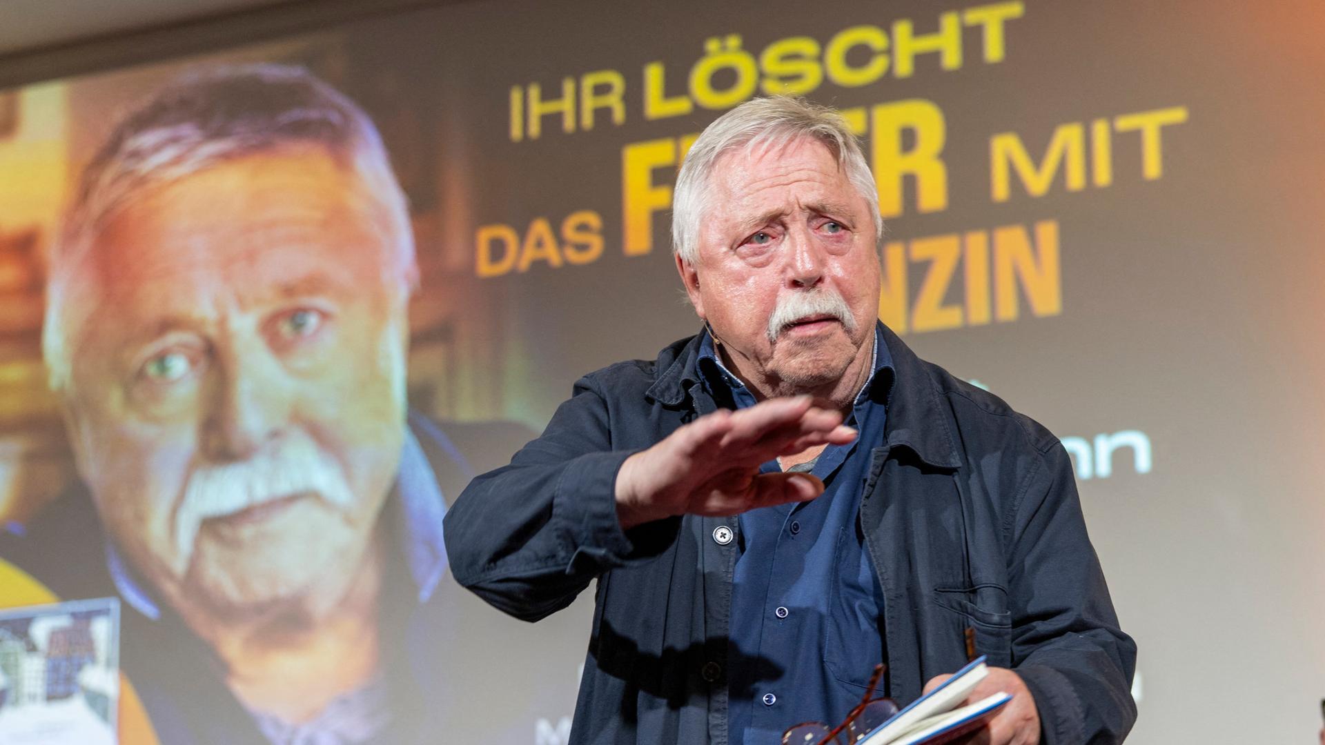 Ein Mann, der Liedermacher und Lyriker Wolf Biermann, steht vor einer Projektion seines eigenen Porträts und dem Schriftzug "Ihr löscht das Feuer mit Benzin" Ein Mann, der Liedermacher und Lyriker Wolf Biermann, steht vor einer Projektion seines eigenen Porträts und dem Schriftzug "Ihr löscht das Feuer mit Benzin"