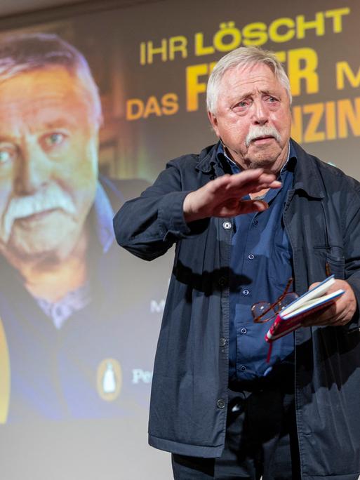 Ein Mann, der Liedermacher und Lyriker Wolf Biermann, steht vor einer Projektion seines eigenen Porträts und dem Schriftzug "Ihr löscht das Feuer mit Benzin"