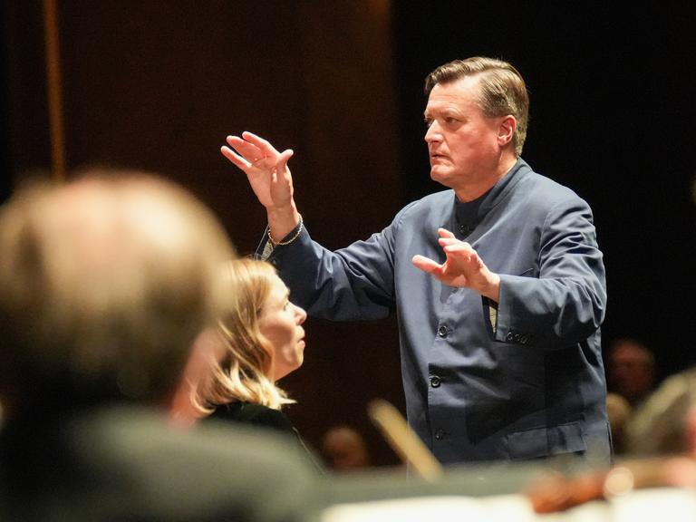 Der Dirigent Christian Thielemann dirigiert konzentriert, im Vordergrund sind mehrere Köpfe von Musikern zu sehen.