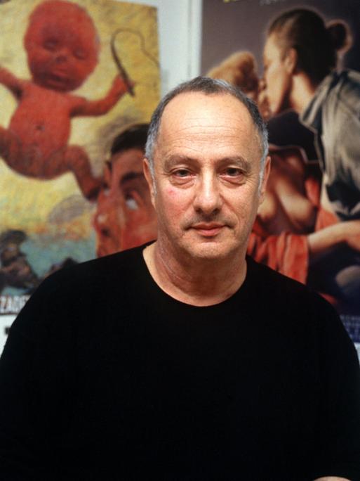 Peter Zadek sitzt vor einer Wand, die mit Fotografien und Plakaten behangen ist.