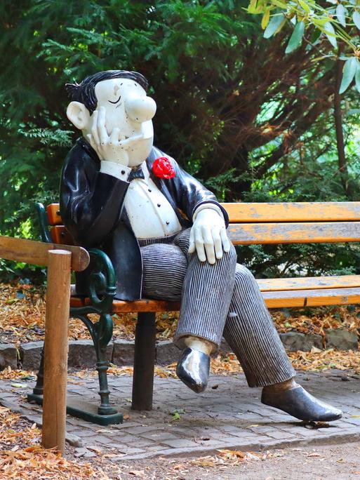 Eine männliche Figur nach den Zeichnungen von Loriot sitzt in Lebensgröße auf einer Parkbank.