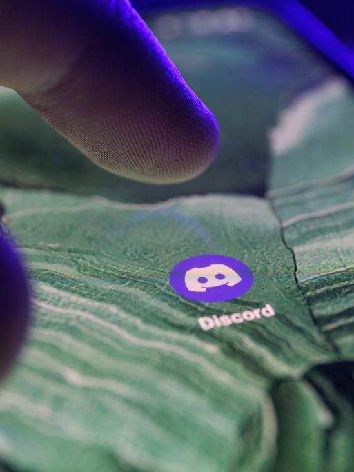 Die Discord App ist auf dem Bildschirm eines Smartphones zu sehen. Ein Finger bewegt sich darauf, um sie anzutippen.
