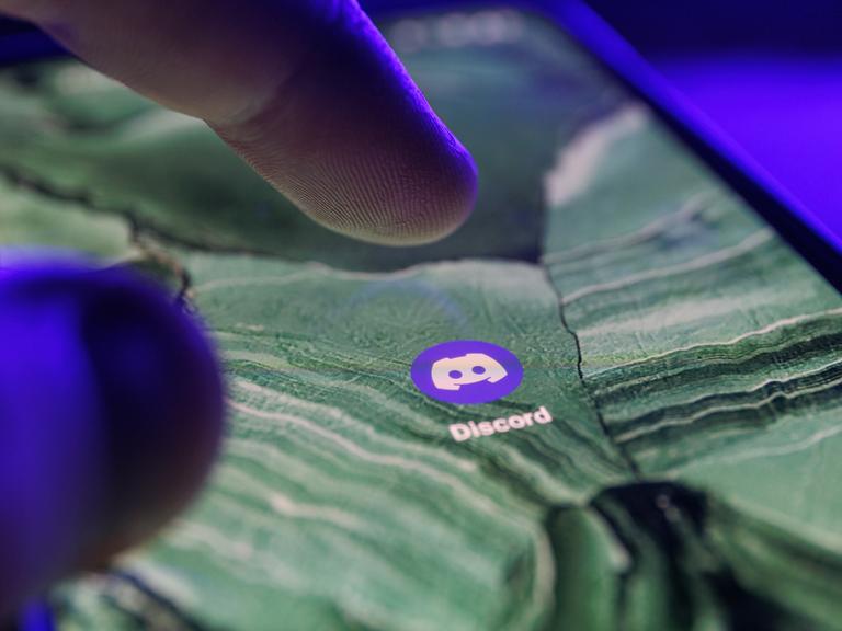Die Discord App ist auf dem Bildschirm eines Smartphones zu sehen. Ein Finger bewegt sich darauf, um sie anzutippen.