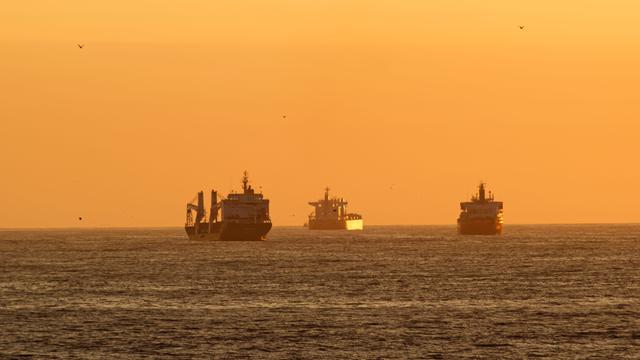 Drei Frachtschiffe im Meer während eines orangefarbenen Sonnenuntergangs.