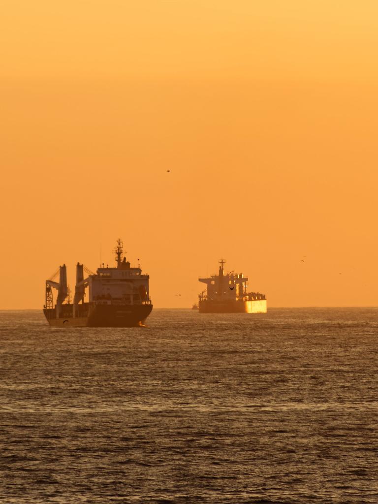 Drei Frachtschiffe im Meer während eines orangefarbenen Sonnenuntergangs.