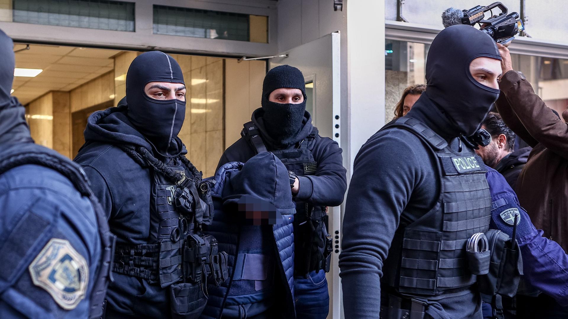 Der Mann wird von maskierten Polizisten aus einem Gebäude geführt. Der Mann wird von maskierten Polizisten aus einem Gebäude geführt.