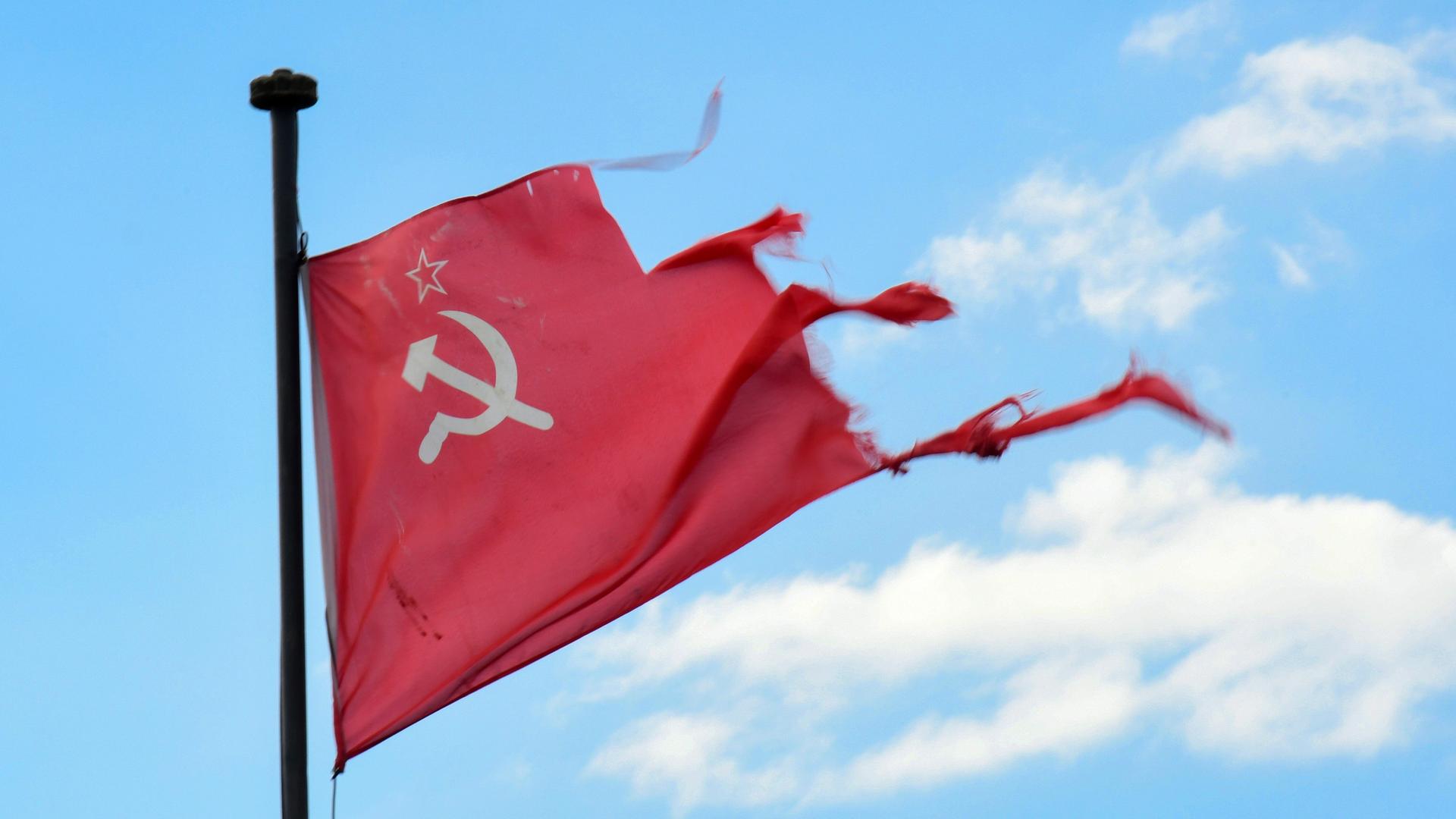 Vor blauem Himmel hängt eine zerrissene sowjetische Flagge mit Hammer, Sichel und Stern. Vor blauem Himmel hängt eine zerrissene sowjetische Flagge mit Hammer, Sichel und Stern.
