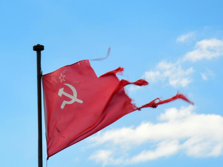 Vor blauem Himmel hängt eine zerrissene sowjetische Flagge mit Hammer, Sichel und Stern.