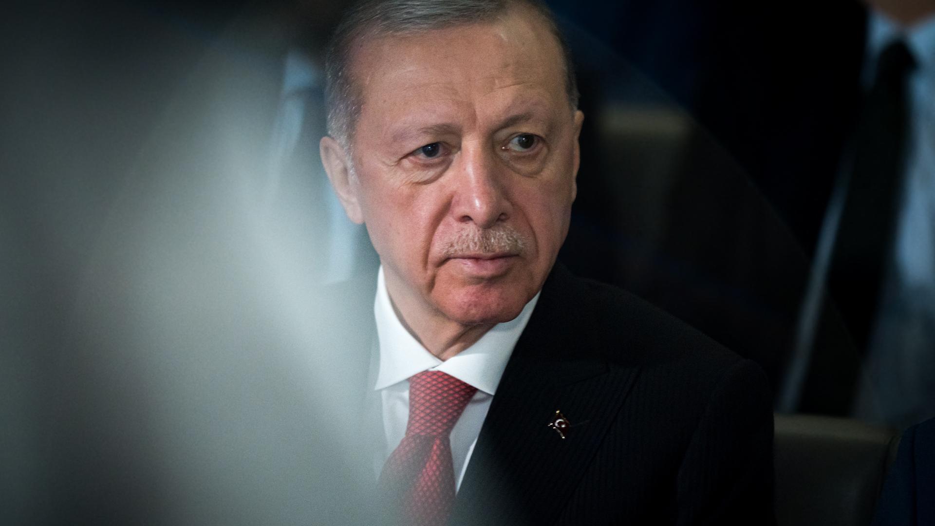 Porträt von Recep Tayyip Erdogan, der ein weißes Hemd, eine rote Krawatte und ein schwarzes Sakko trägt und an der Kamera vorbeischaut.
