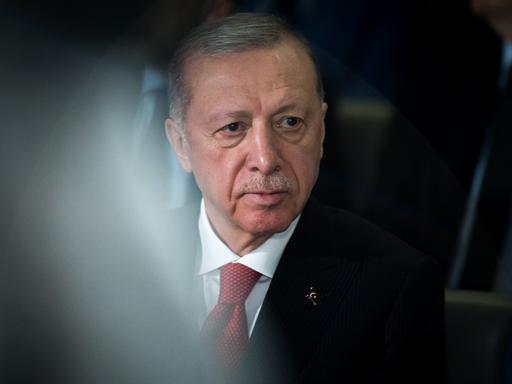 Porträt von Recep Tayyip Erdogan, der ein weißes Hemd, eine rote Krawatte und ein schwarzes Sakko trägt und an der Kamera vorbeischaut.